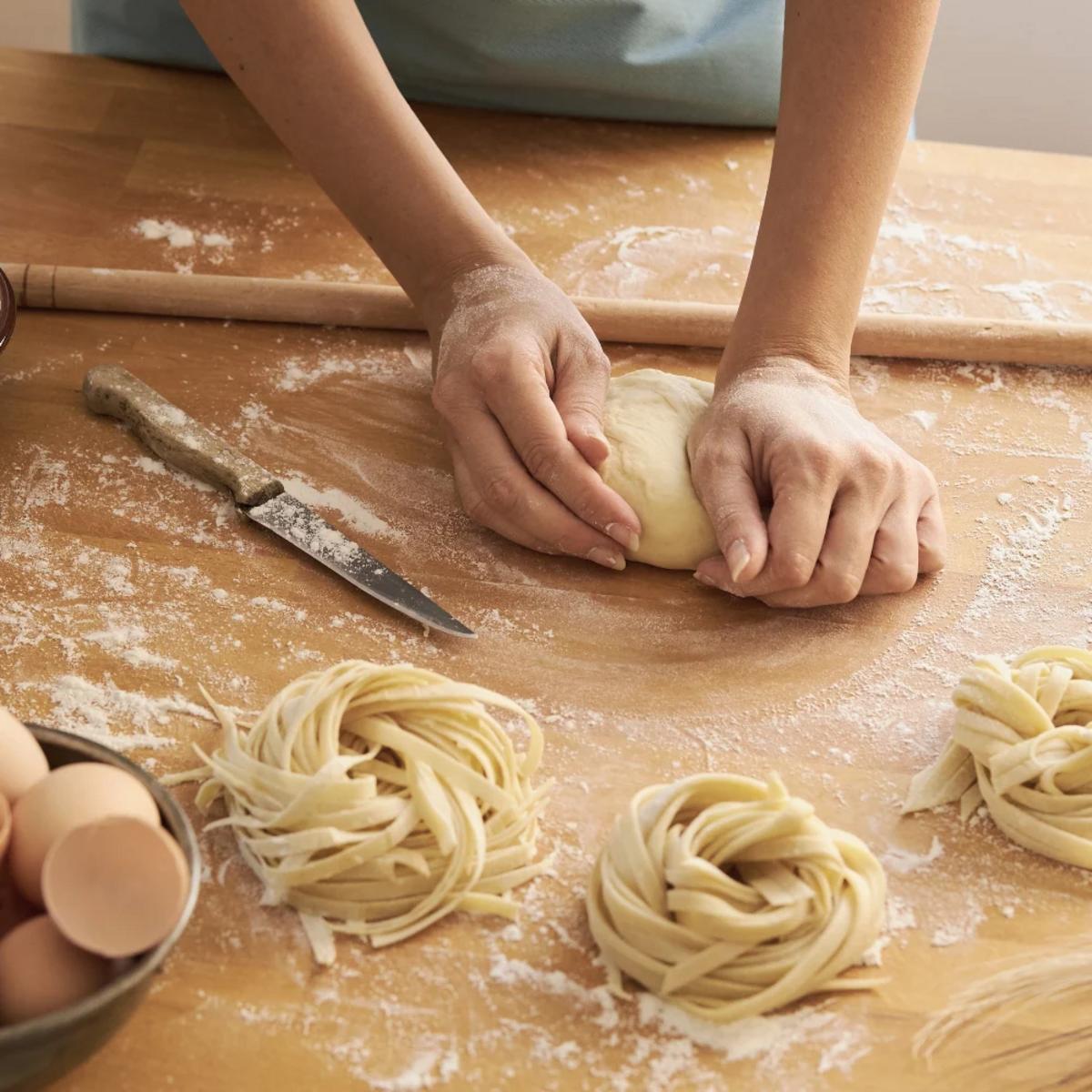 Hands kneading pasta dough on a wooden board